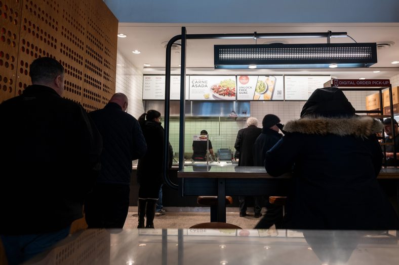 A photo of customers waiting in line inside a Chipotle store