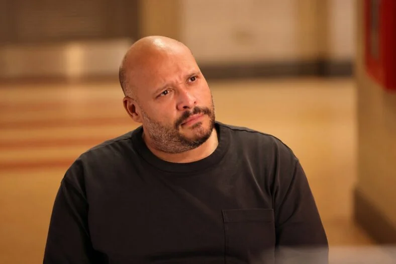 Close up shot of Joe Minoso as Joe Cruz wearing a long sleeve black pocket t-shirt with a pensive expression.