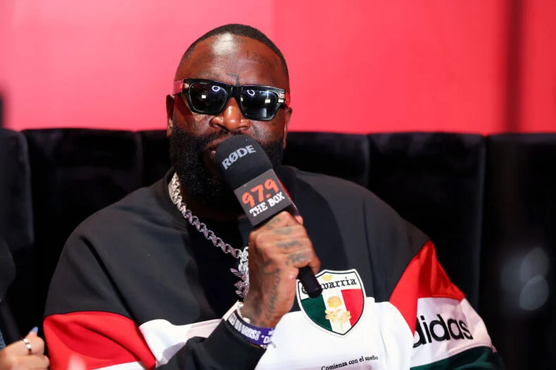 Rick Ross sitting down speaking into a microphone at an event in 2026
