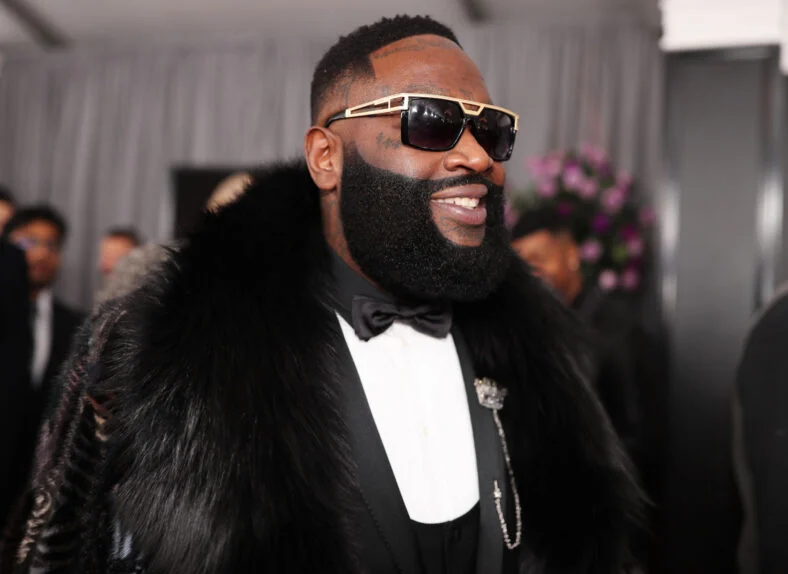 Rick Ross smiling looking to the side on a red carpet in a stock image