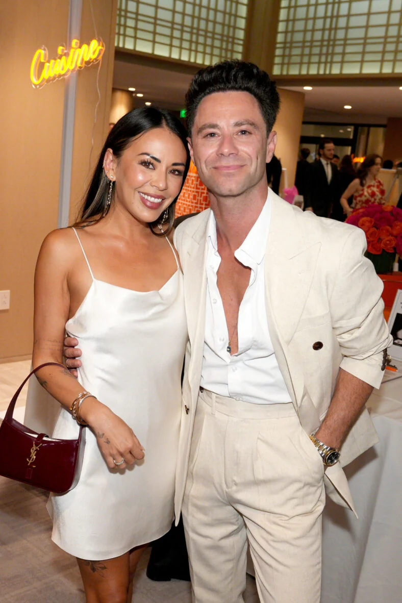 Janel Parrish and Sasha Farber at an event coordinating in white clothes. They are standing together and smiling for the camera